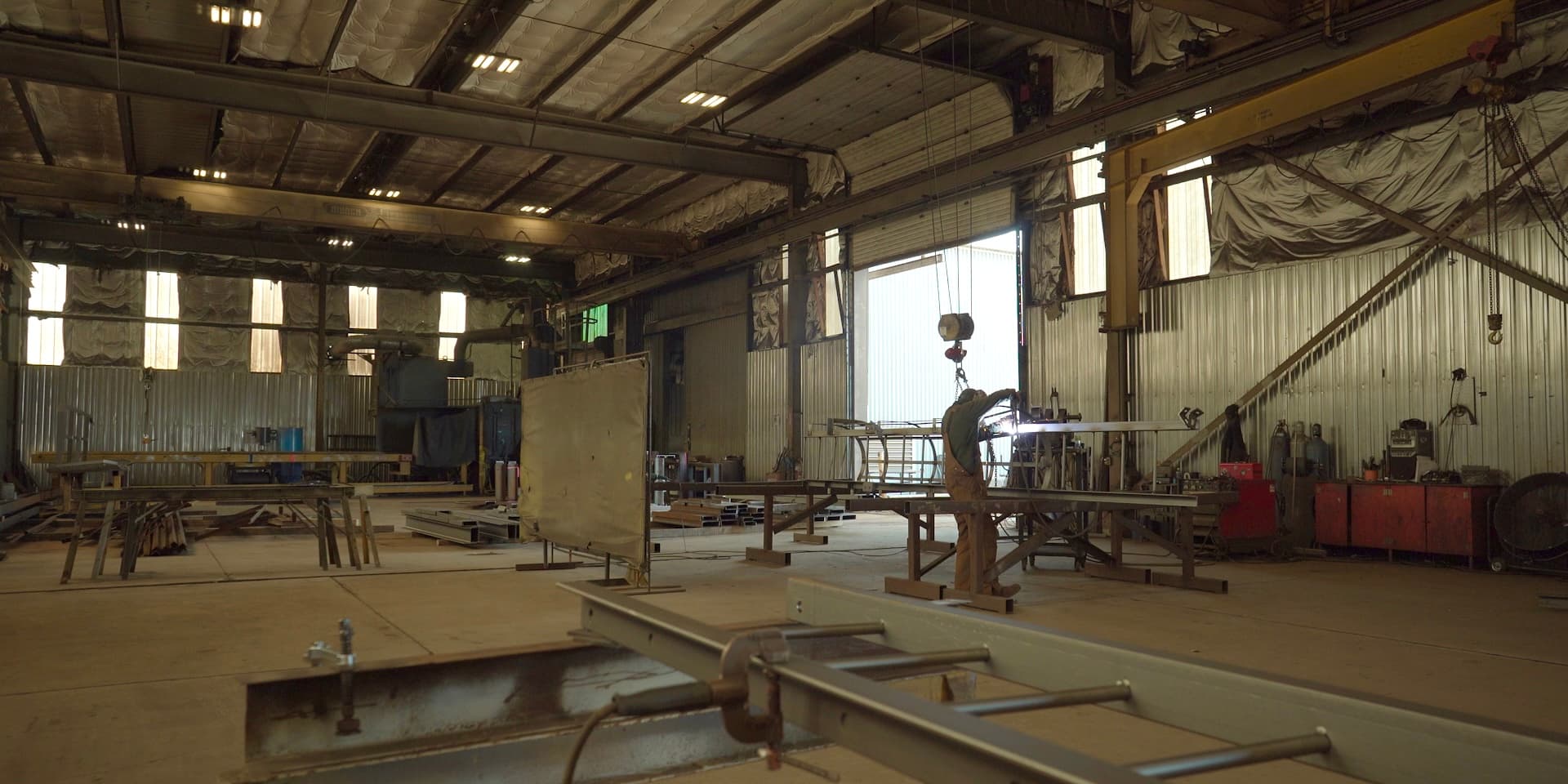 Fabrication bay with welding in progress under overhead crane